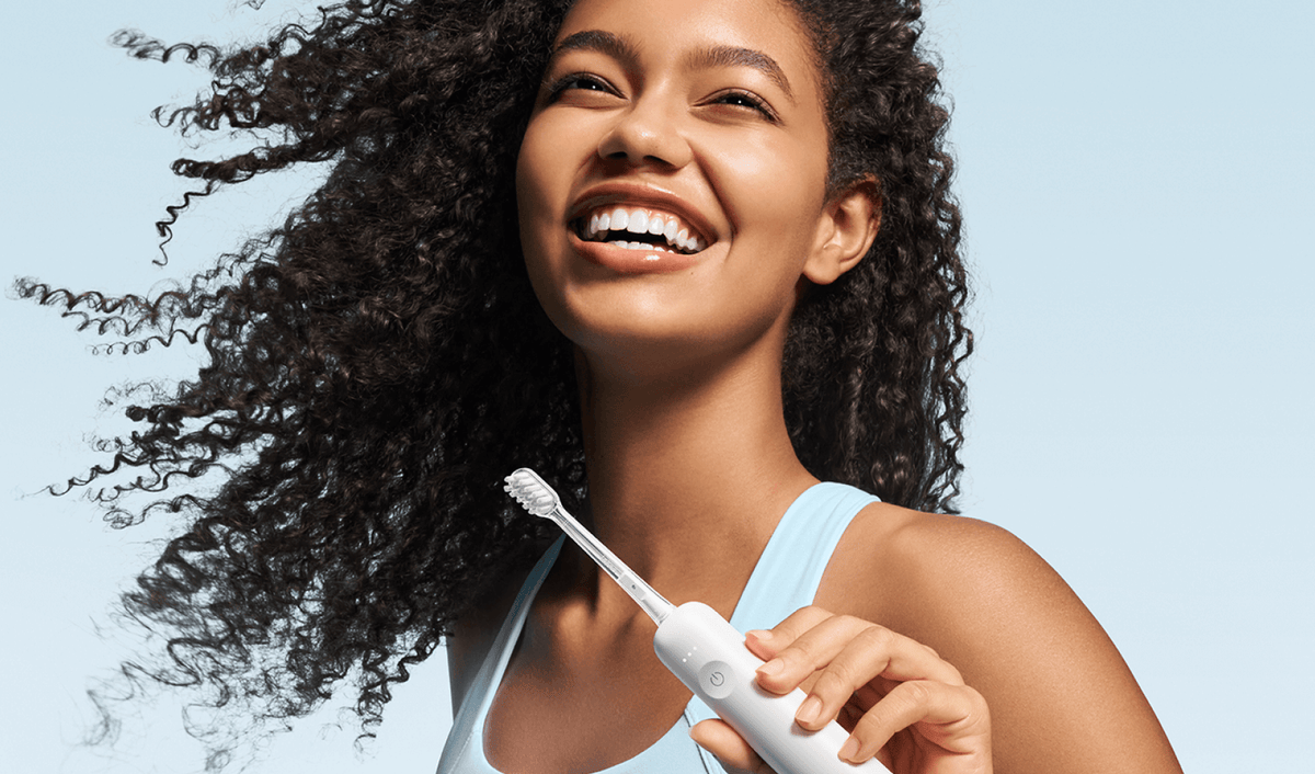 Woman holding a white electric toothbrush against a light blue background