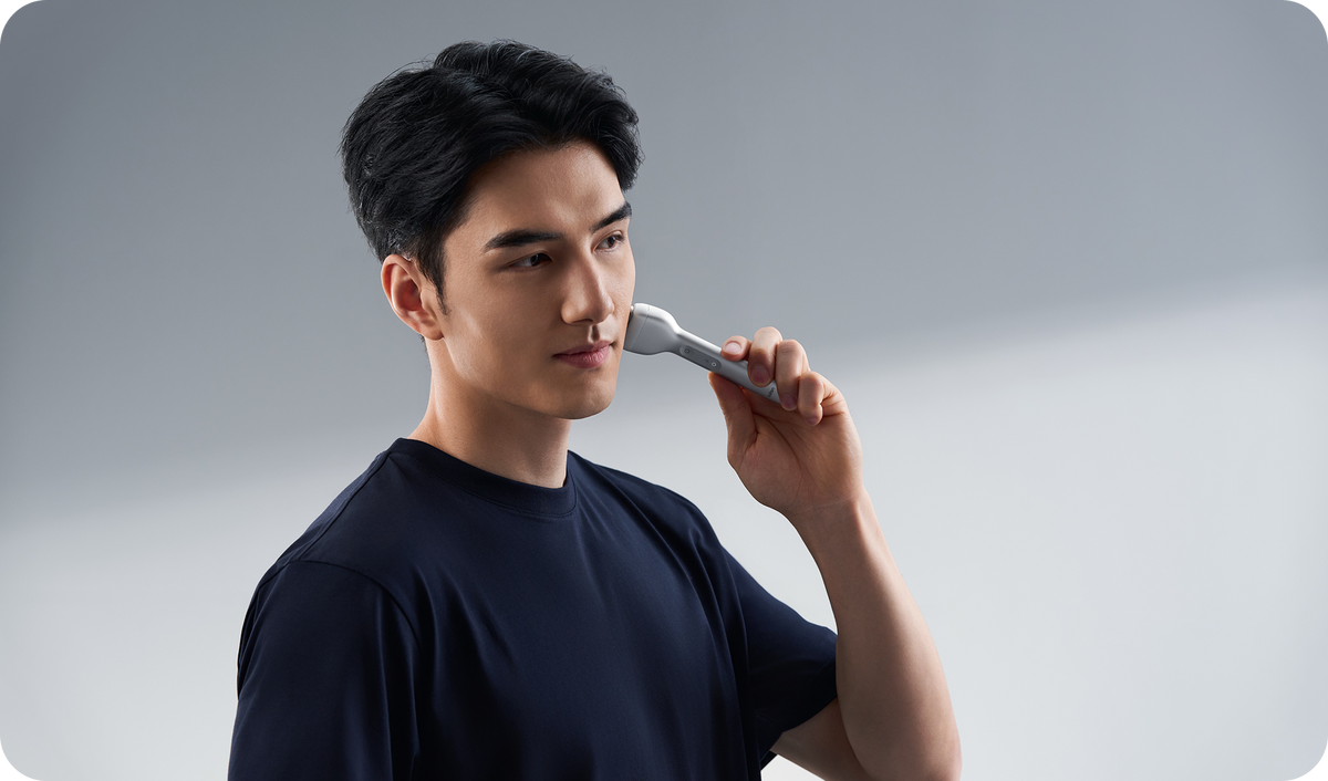 Man holding a white electric toothbrush against a gray background