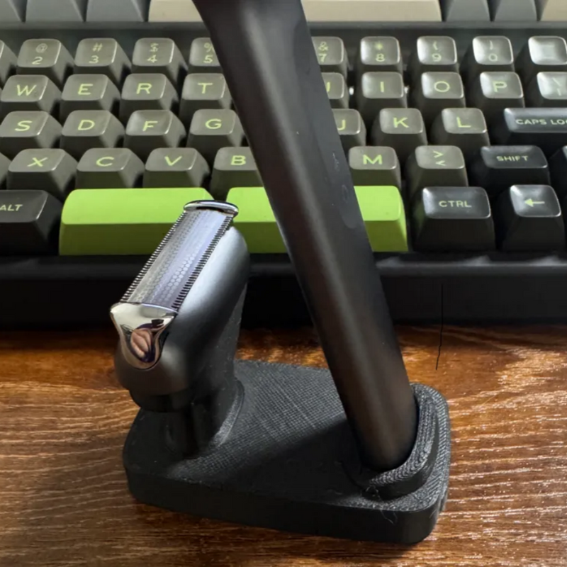 Black stand with a razor on a wooden surface in front of a keyboard